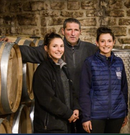 Trois vignerons souriants dans une cave avec des tonneaux